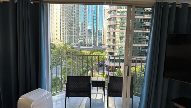 A balcony with two chairs, a white appliance, and a view of tall buildings. - 2-bedroom apartment in Waikiki with PARKING included (Honolulu)