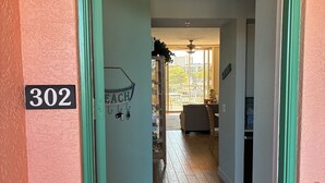 Um corredor com a placa de número '302' na parede, que leva a um quarto com ventilador de teto e vista para o exterior.