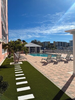 A pool area with lounge chairs, a small pool, and a paved walkway with artificial grass. - Daily BEACH WALKS! Relax by the pool. Spacious 2-bedroom condo Fort Myers Beach (Fort Myers Beach)