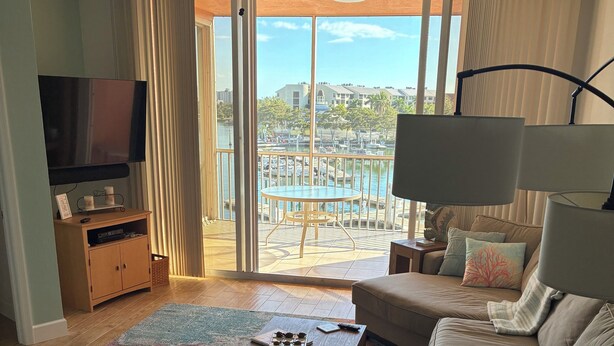 Sala de estar com sofá, mesa de centro, televisão e varanda com vista para a cidade.