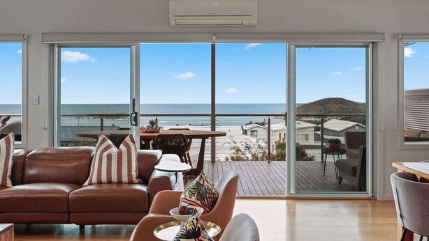 Ein geräumiges Wohnzimmer mit einem großen Schiebeglasfenster, das auf einen Balkon mit Blick auf den Strand führt.