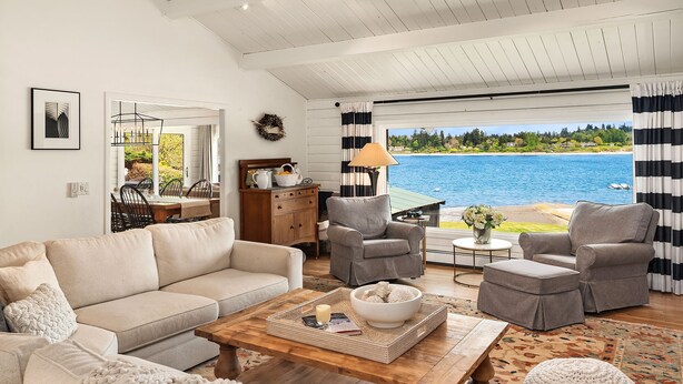 Ein Wohnzimmer mit einer Couch, Sesseln, einem Couchtisch und Blick auf einen See.
