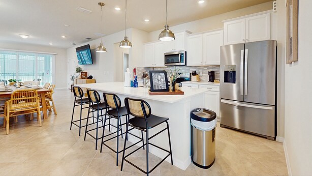 A modern kitchen with white cabinets, stainless steel appliances, and a central island with bar stools. - Amazing home with outdoor patio, wifi, & close to local attractions near Orlando (Clermont)