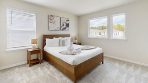 A bedroom with a wooden bed, two bedside tables, a nightstand, and a window with blinds. - Amazing home with outdoor patio, wifi, & close to local attractions near Orlando (Clermont)