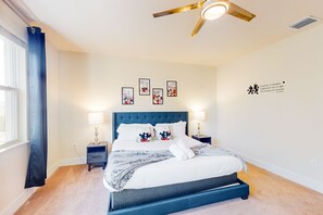Un lit bien fait, avec une tête de lit bleue, deux tables de chevet avec des lampes et des œuvres d’art accrochées au mur au-dessus du lit.
