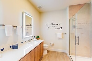 Une salle de bain moderne avec un grand miroir, un meuble-lavabo doté d’un plan de toilette blanc, des toilettes et une douche à parois de verre.