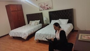 A hotel room with two beds, a ceiling fan, a wooden wardrobe, and a painting on the wall. - Flor y Canto  (Matehuala)