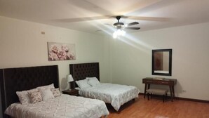 A bedroom with two beds, a desk, a ceiling fan, and a wall-mounted mirror. - Flor y Canto  (Matehuala)