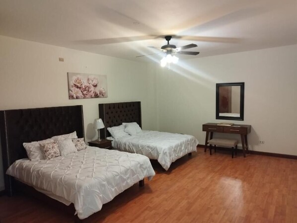 A bedroom with two beds, a desk, a ceiling fan, and a wall-mounted mirror. - Flor y Canto (Matehuala)