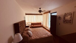 A hotel room with a bed, a sofa, a ceiling fan, and a window with curtains. - Flor y Canto  (Matehuala)