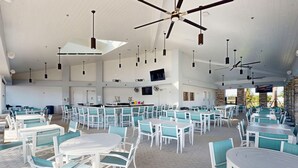 A spacious indoor dining area with multiple tables and chairs, ceiling fans, and a kitchen area in the background. - Contemporary townhouse w/ private pool and resort amenities, near attractions (Clermont)