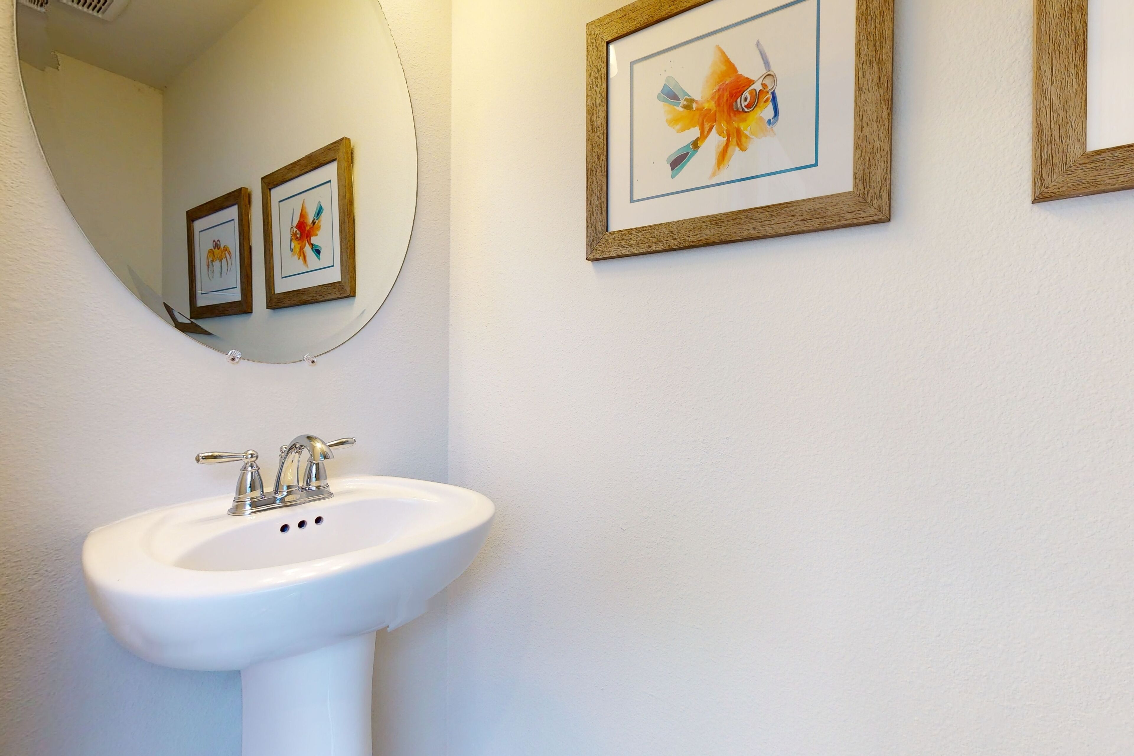 A bathroom with a white sink, a mirror, and two framed pictures on the wall.