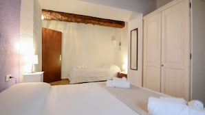 Ein Hotelzimmer mit einem großen Bett, einem kleineren Bett, einem Schrank und einem Nachttisch mit Lampe.