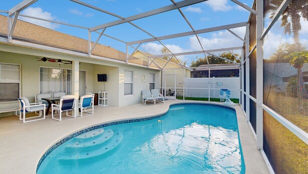 A covered swimming pool with lounge chairs and a table, surrounded by a white fence. - Spacious Retreat with Private Pool, Enclosed Yard, WiFi & Game Room (Clermont)