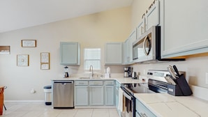 A modern kitchen with light blue cabinets, a stainless steel dishwasher, a built-in oven, and a microwave. There are framed pictures on the wall and a window above the sink. - Spacious Retreat with Private Pool, Enclosed Yard, WiFi & Game Room (Clermont)