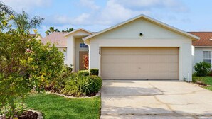 A single-story house with a garage, a front yard with various plants, and a clear sky. - Spacious Retreat with Private Pool, Enclosed Yard, WiFi & Game Room (Clermont)