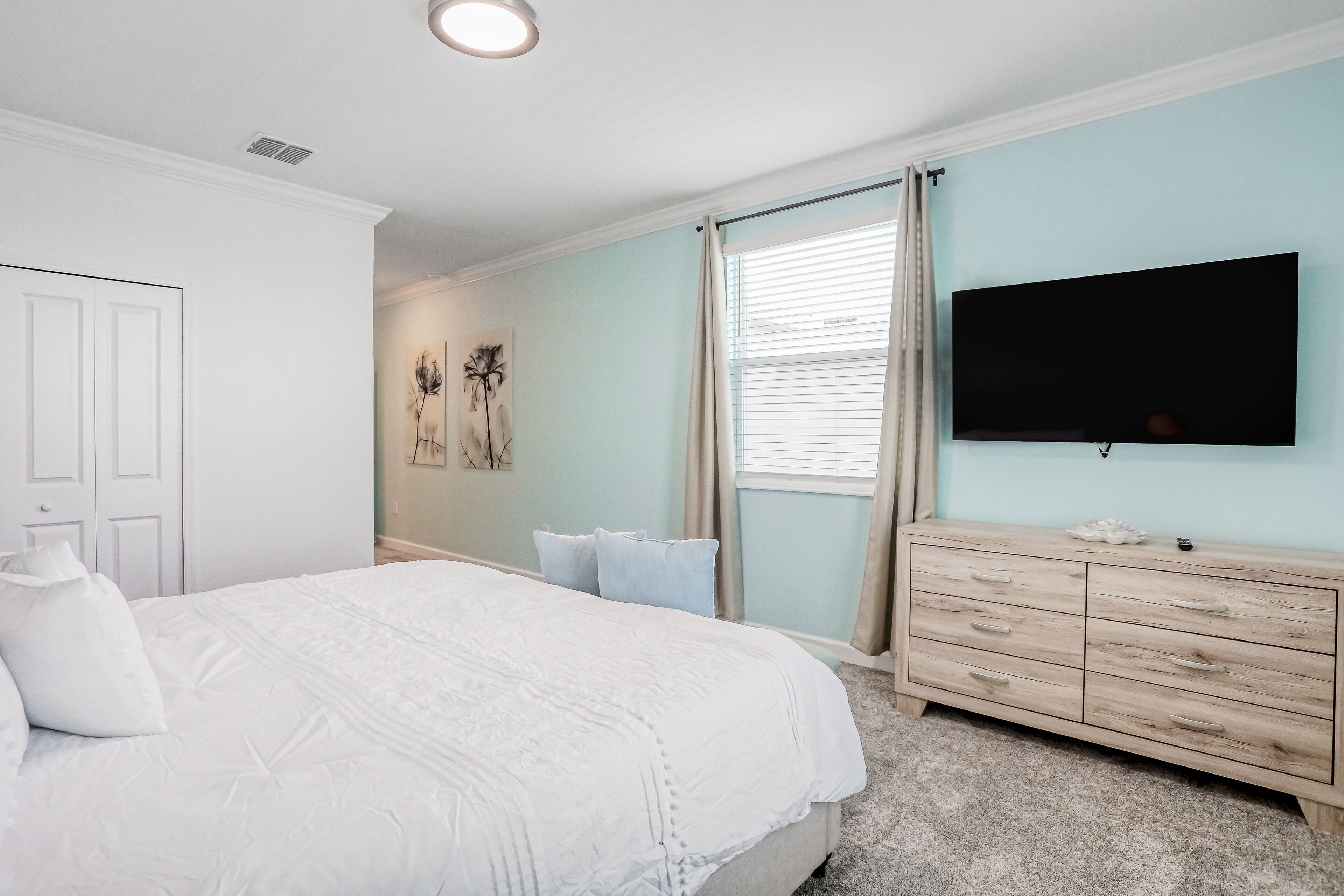 A bedroom with a bed, a dresser, a TV, and a window with curtains.