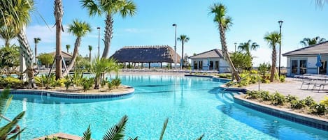 Ein Swimmingpool mit einer strohgedeckten Struktur im Hintergrund, umgeben von Palmen und Liegestühlen.
