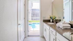 Un baño con un espejo grande, dos lavamanos y vistas a una piscina a través de una puerta abierta.