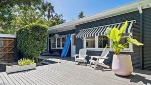 Une terrasse en bois avec des chaises blanches, une planche de surf et une plante en pot.