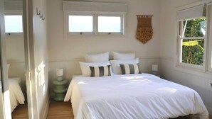 Une chambre à coucher avec un lit, deux tables de chevet, une fenêtre et un miroir.