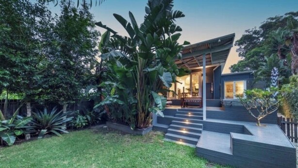 Une maison moderne dotée d’un grand jardin à l’avant, d’un escalier menant à l’entrée et d’une végétation luxuriante qui entoure la propriété.