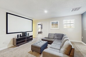 Ein Wohnzimmer mit einem großen Flachbildfernseher, einem Ecksofa und einem kleinen Hocker.
