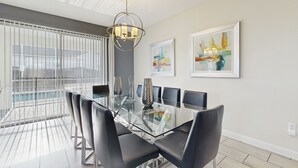 A modern dining area with a glass table and black chairs, a chandelier, and two abstract paintings on the wall.