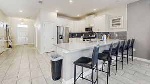 A modern kitchen with white cabinets, a central island with bar stools, a stainless steel refrigerator, and a microwave.