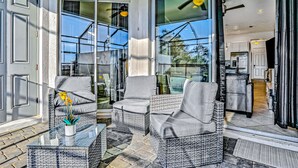 Eine sonnendurchflutete Terrasse mit Korbmöbeln, eine Glastür zu einer Küche und ein Topf mit Pflanze auf einem Glastisch.