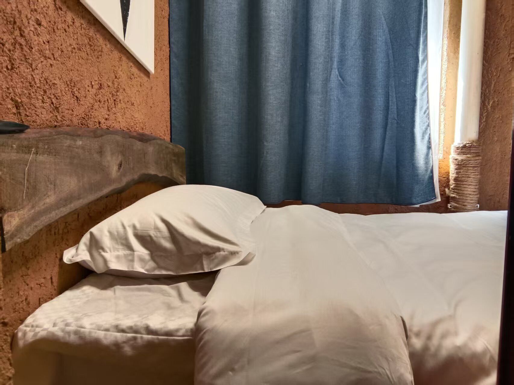 Una cama con ropa de cama blanca, cabecera de madera y cortina azul.