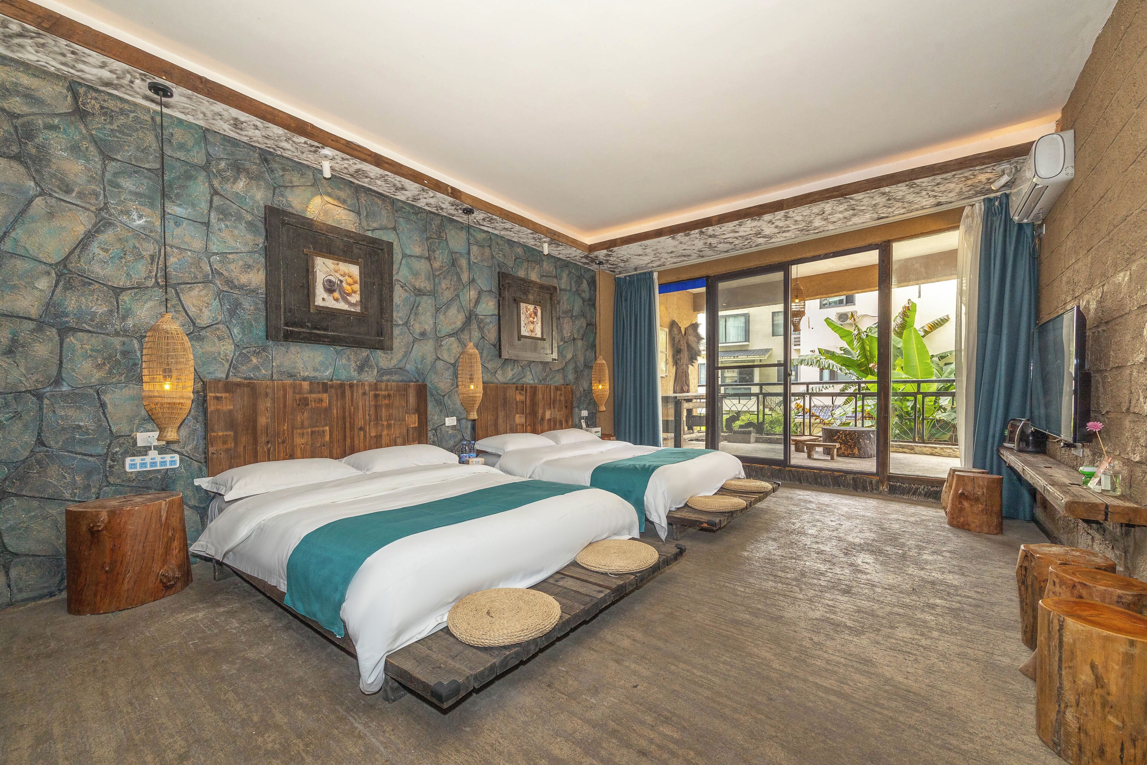 Een hotelkamer met een stenen muur, twee bedden met witte lakens, een houten vloer en uitzicht op het omliggende landschap via een glazen deur.