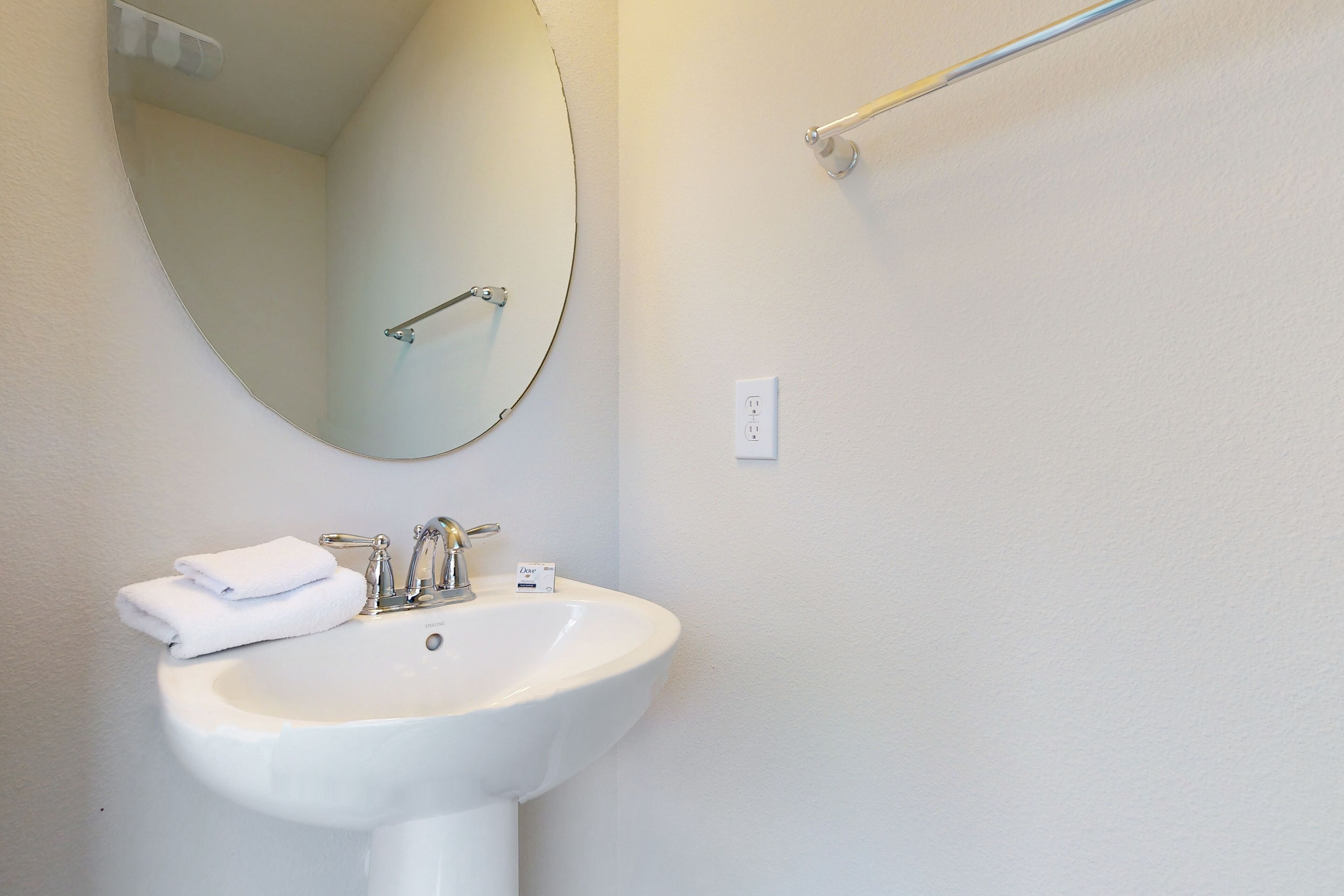 Un baño con un lavabo blanco, un espejo y un perchero para toallas.
