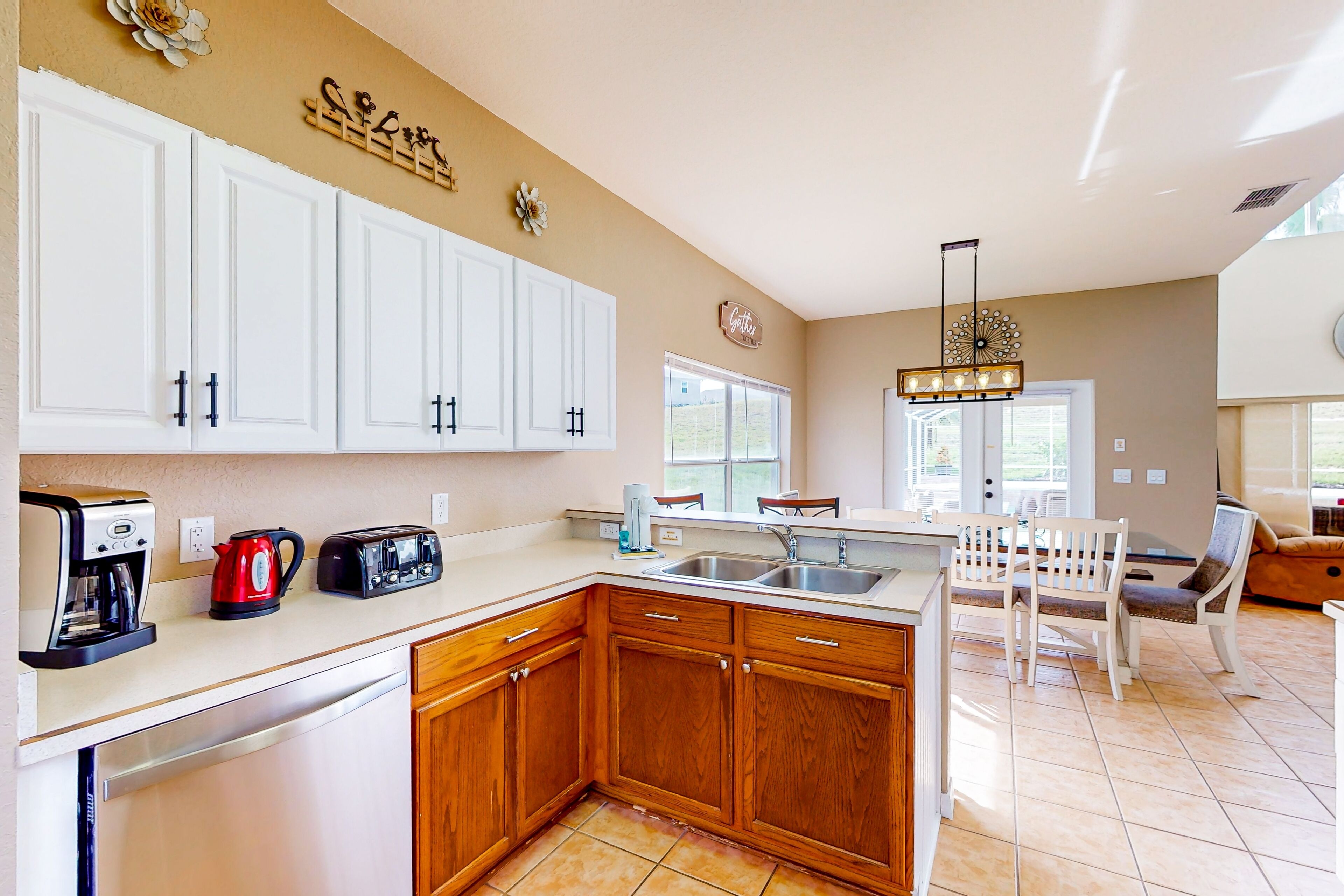 A kitchen with white cabinets, a coffee maker, a toaster, and a sink. There is a dining area with a table and chairs.