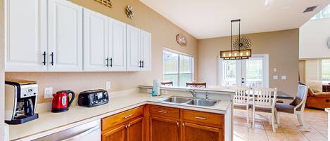 A kitchen with white cabinets, a coffee maker, a toaster, and a sink. There is a dining area with a table and chairs.