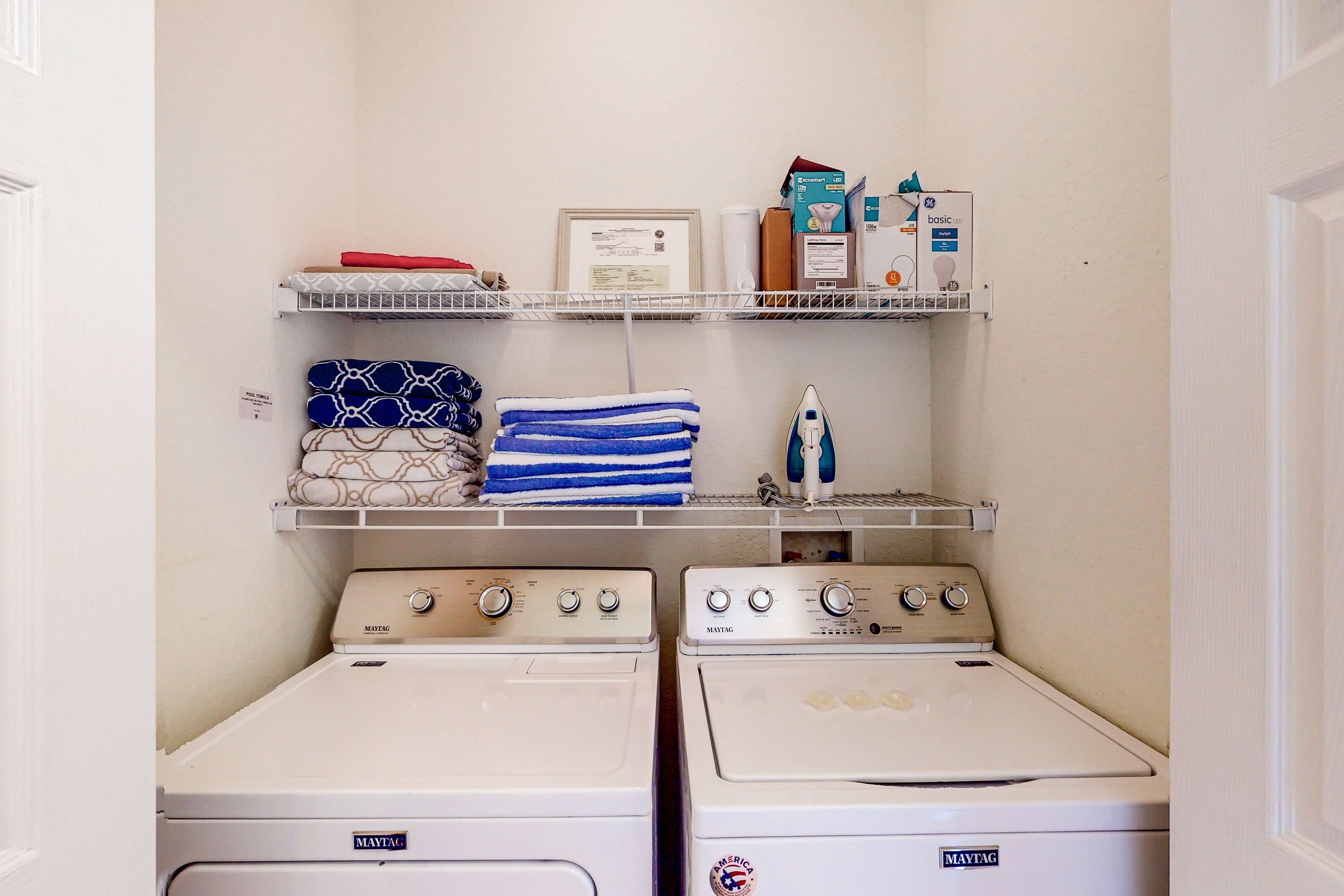 Un espace dédié à la buanderie, comprenant deux machines à laver Maytag, une étagère avec des serviettes pliées, un certificat encadré et des produits de lessive.