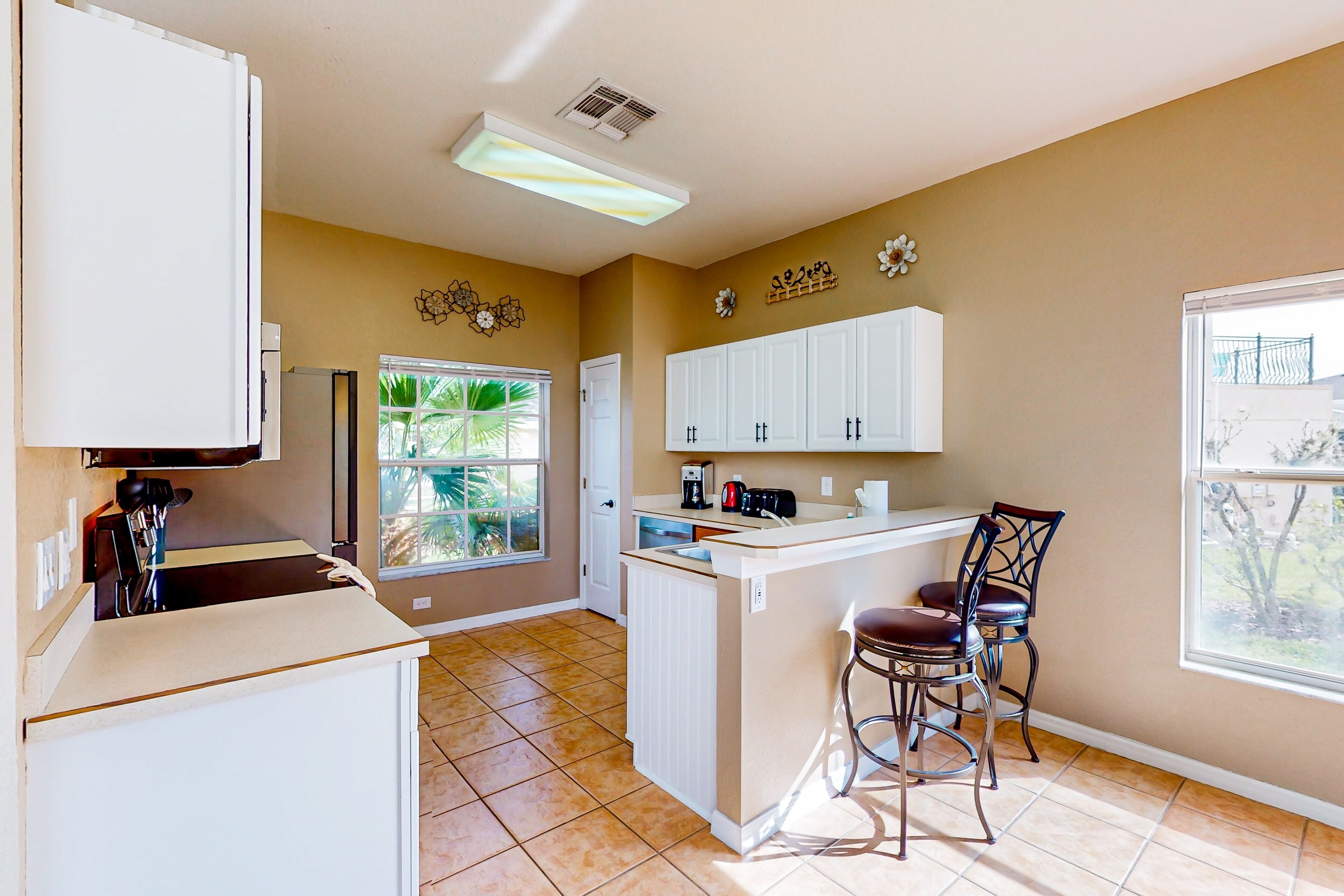 A kitchen with white cabinets, a countertop, a coffee maker, and a window with a view of greenery.