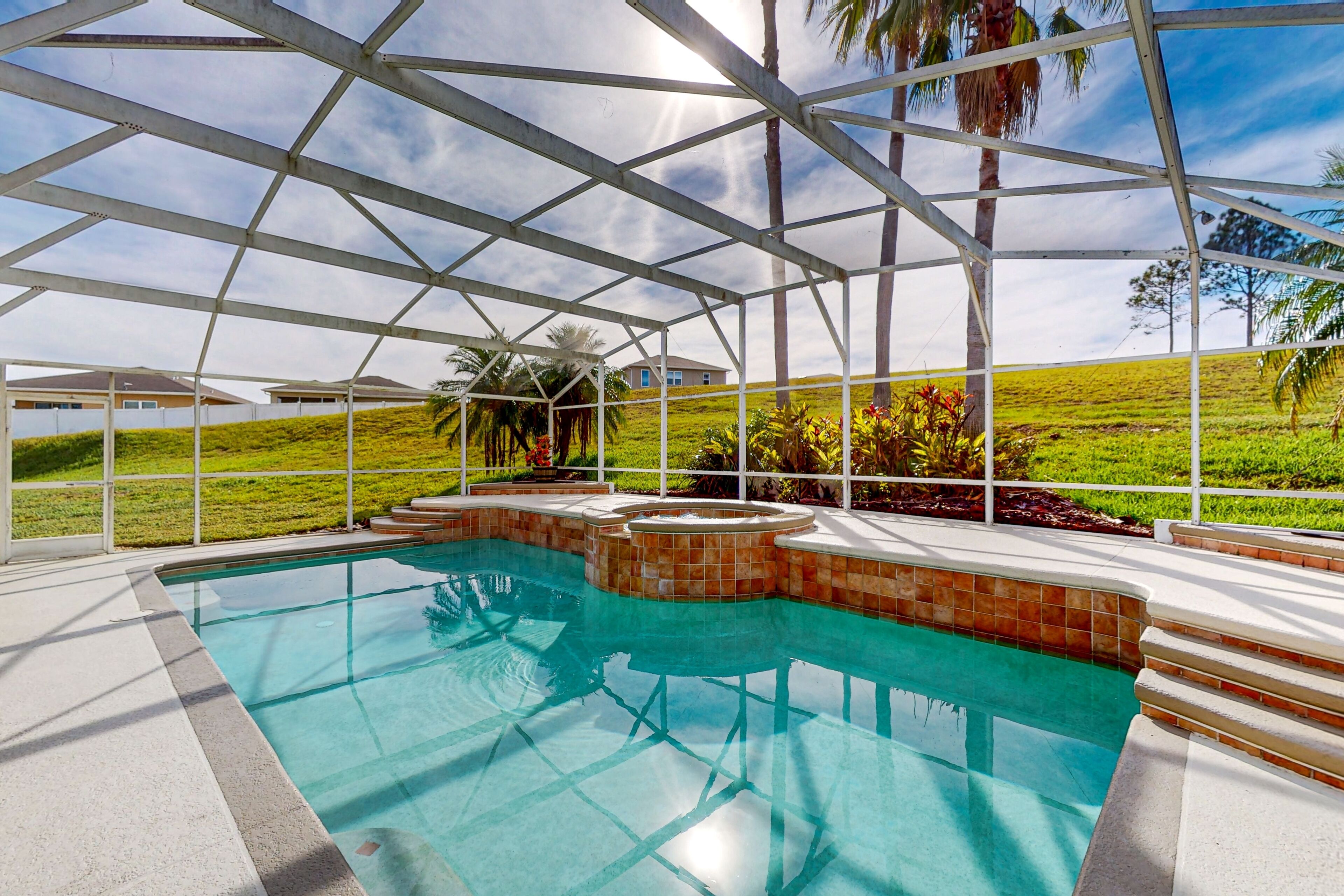 Ein Swimmingpool mit klarem, blauem Wasser, umgeben von einer weißen Metallkonstruktion und einer grünen Landschaft mit Palmen im Hintergrund.
