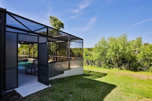 A modern glass-enclosed structure with a pool and outdoor seating, surrounded by greenery.