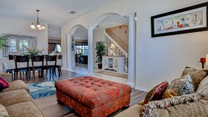 A spacious living room with a red ottoman, a dining area with a table and chairs, and a staircase leading to another level. - Stunning house with lanai, pool, ping-pong, full kitchen, & WiFi (Davenport)