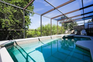An indoor swimming pool with clear blue water, surrounded by a metal frame and glass panels, and shaded by a blue canopy.