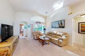A spacious living room with a large flat-screen TV, a beige leather sofa, a round coffee table, and a framed painting of sailboats. - Snowbird-friendly home near Disney with private pool, lanai, tennis, basketball (Davenport)
