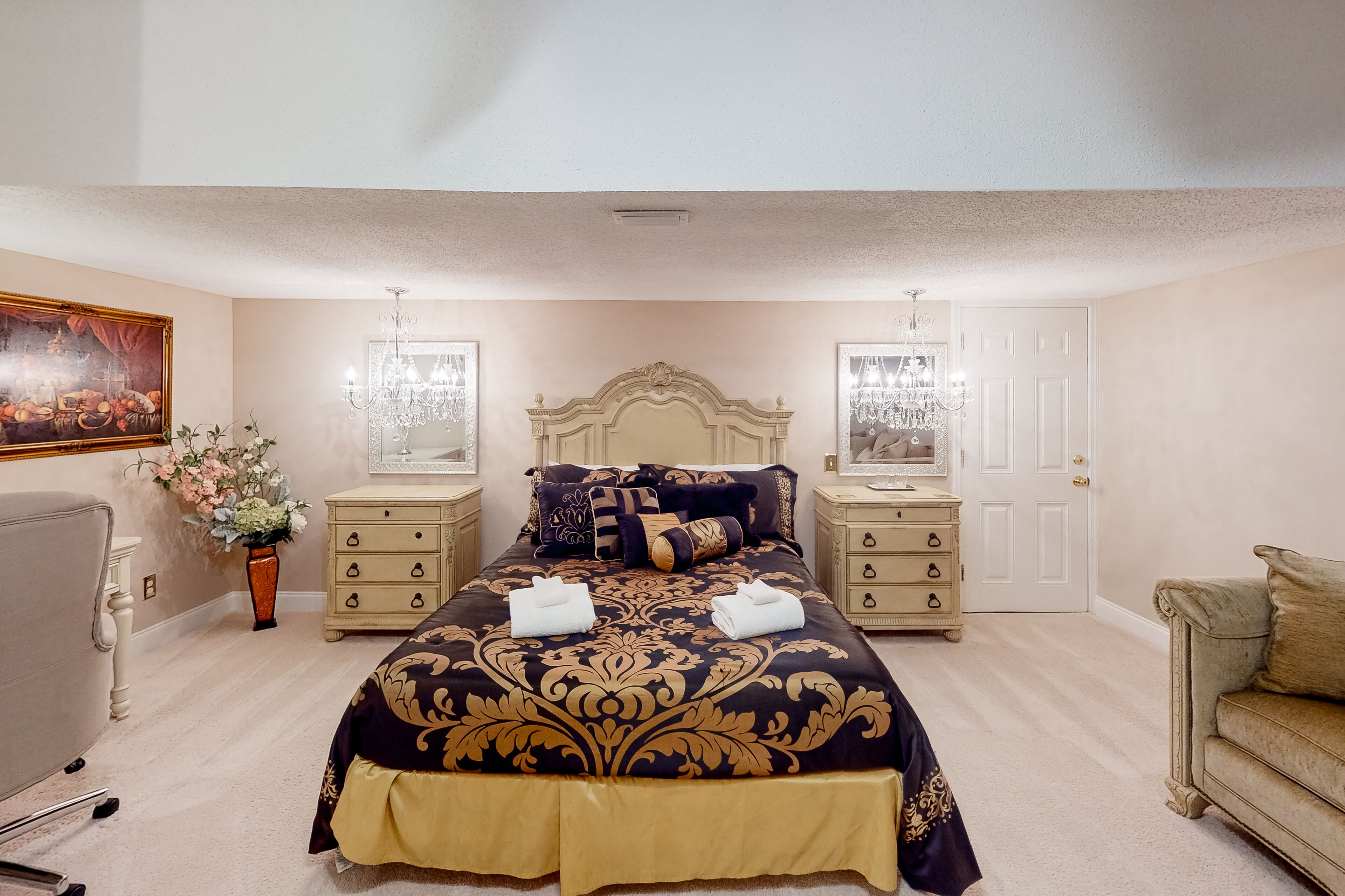 A bedroom with a large bed, two bedside tables, a dresser, a chair, and a painting on the wall.