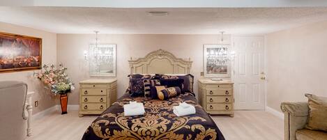 A bedroom with a large bed, two bedside tables, a dresser, a chair, and a painting on the wall.