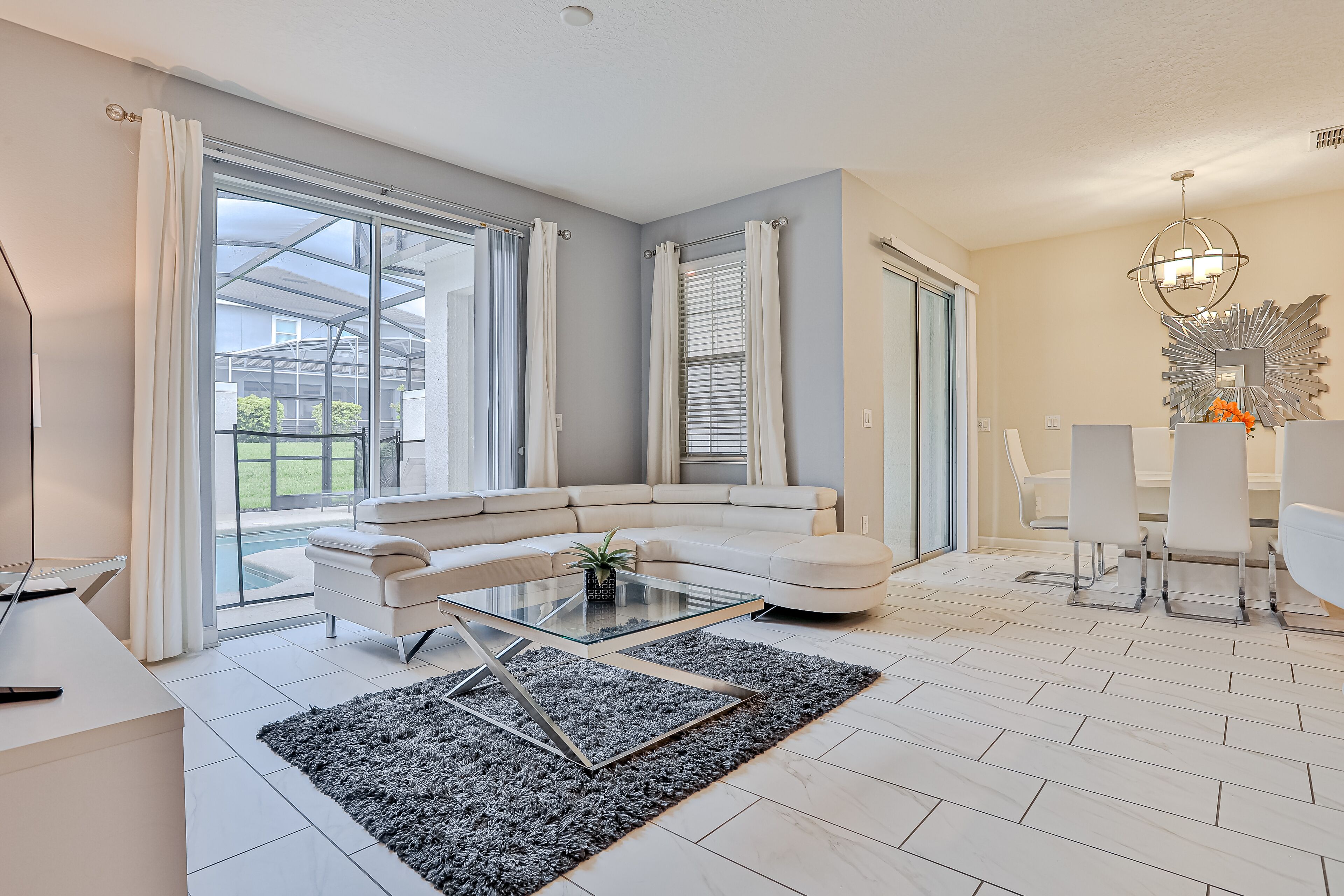 Un salon moderne avec un canapé blanc, une table basse en verre et un coin repas avec des chaises blanches.