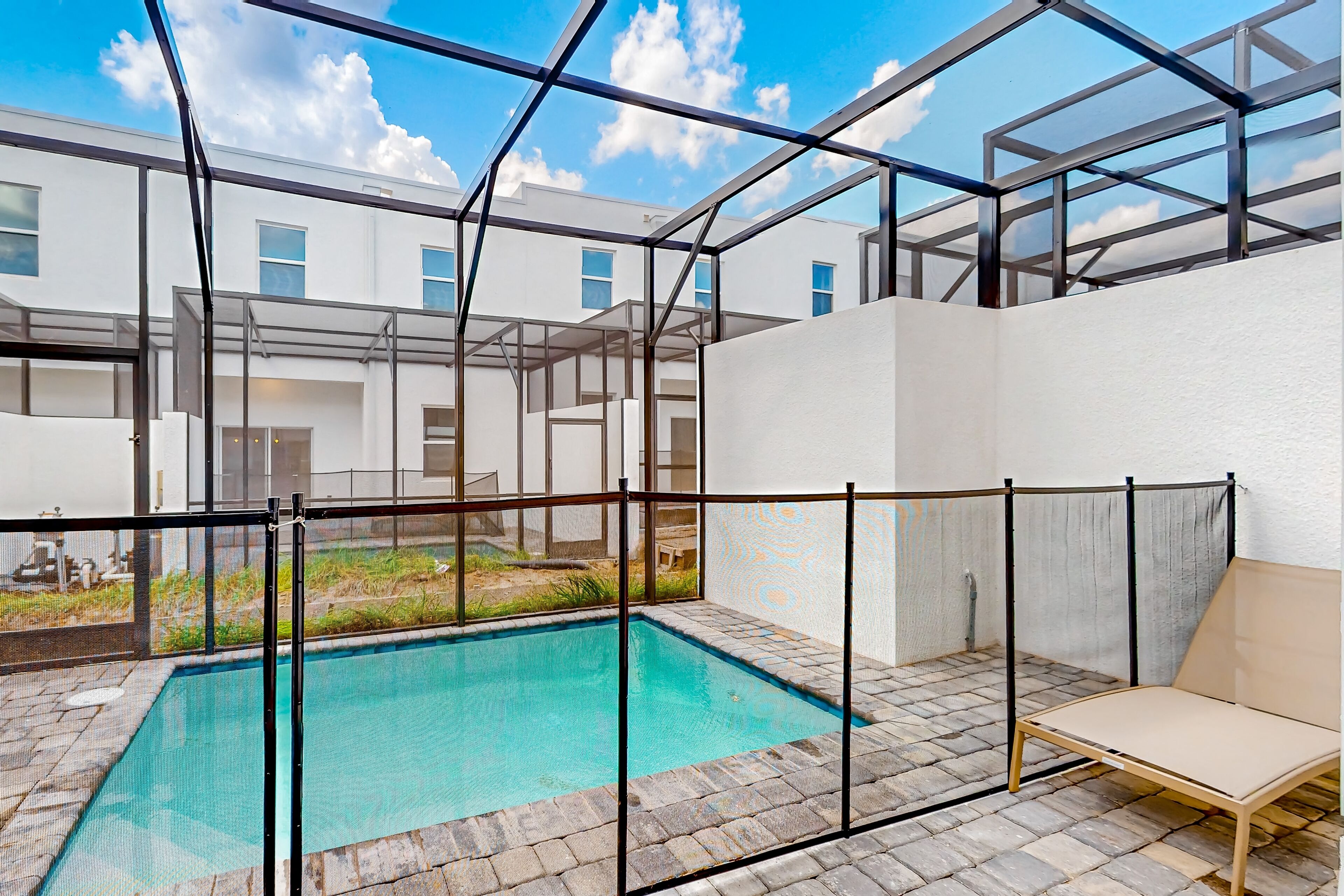 Un espace piscine extérieur moderne, doté d’une structure en verre, d’une chaise longue et offrant une vue sur les bâtiments environnants.