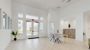 En rummelig, moderne hotellobby med store vinduer, en receptionsdisk og en brandslukker.