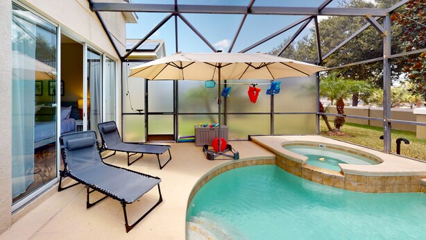 A covered outdoor swimming pool area with lounge chairs, a hot tub, and an umbrella. - Harmony Villa | Family-friendly home in Davenport with a game room & pool (Davenport)