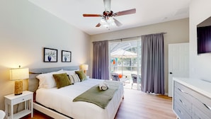 A modern bedroom with a bed, bedside tables, a ceiling fan, and a view of an outdoor area with a table and chairs. - Harmony Villa | Family-friendly home in Davenport with a game room & pool (Davenport)