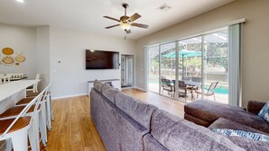A modern living room with a large sofa, a dining area with a white table and chairs, and a ceiling fan. - Harmony Villa | Family-friendly home in Davenport with a game room & pool (Davenport)